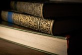 In Nahaufnahme sind drei übereinanderliegende, historische Bücher zu sehen. Das unterste Buch liegt so, dass die Seiten nach vorne zeigen. Die beiden oberen Bände zeigen ihren verschnörkelt verzierten Rücken.